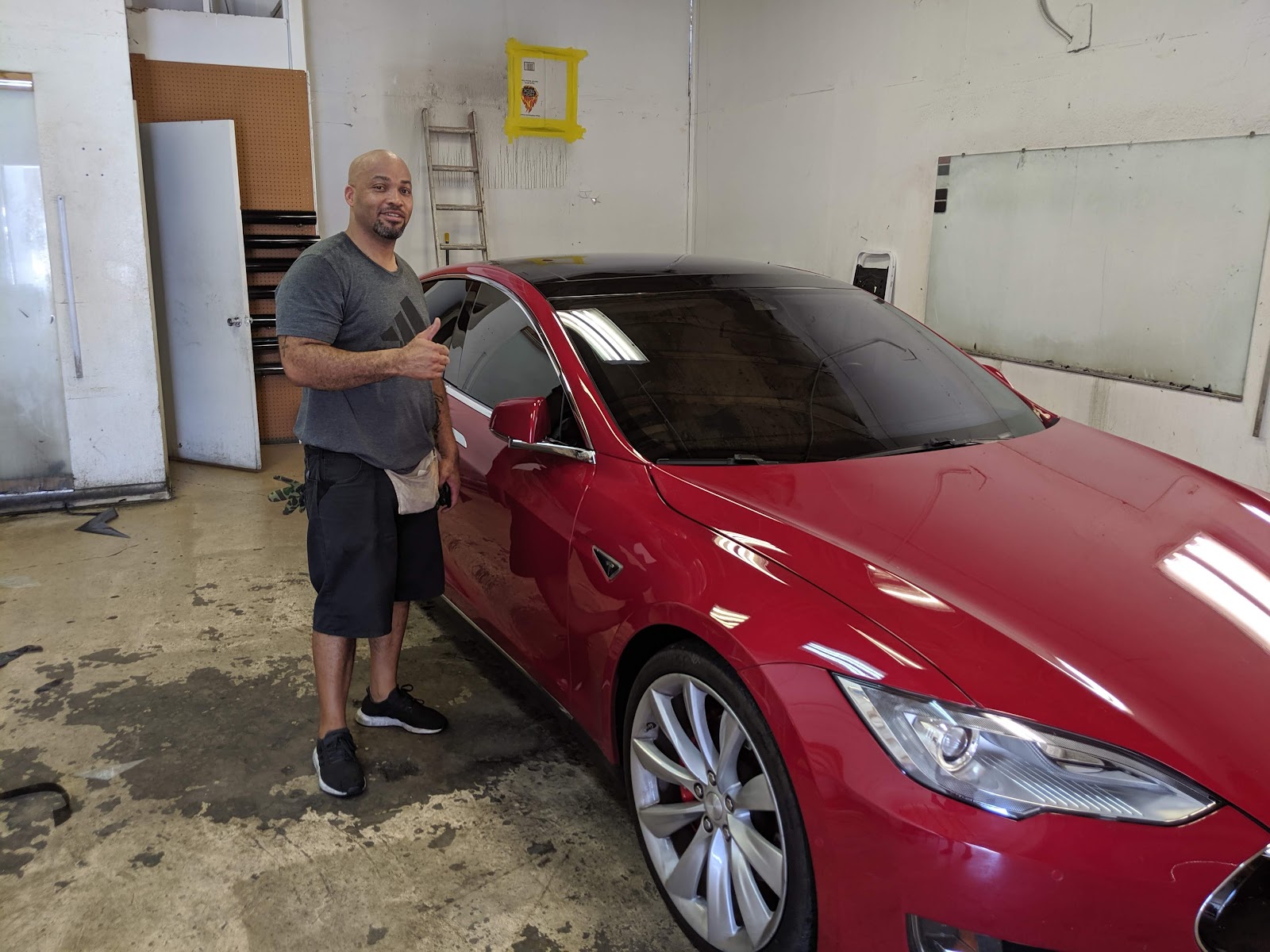 Smiling customer giving a thumbs up next to a red Tesla Model S with tinted windows